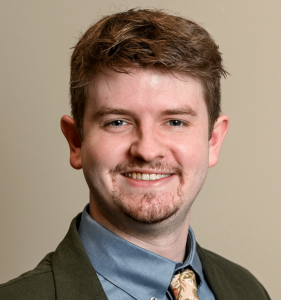 Micah Johnston poses for a standard headshot wearing a green jacket and tie.